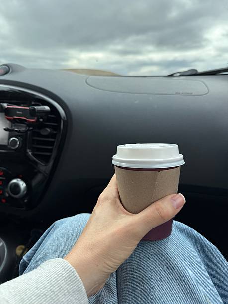 Person holding coffee cup inside a car with sky view from window