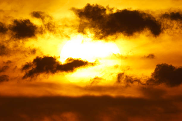 A sun is in the sky with clouds in the background. The sun is yellow and the clouds are white