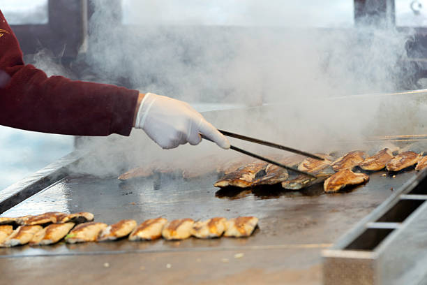 A street vendor grilling fresh fish fillets on a hot metal griddle to prepare traditional fish sandwiches in Istanbul, Turkey. Steam rises as an unrecognizable person wearing gloves cooks seafood at a popular street food stand.
