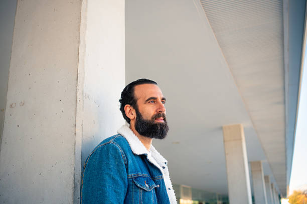 Young adult man leaning against a concrete pillar looking away and thinking