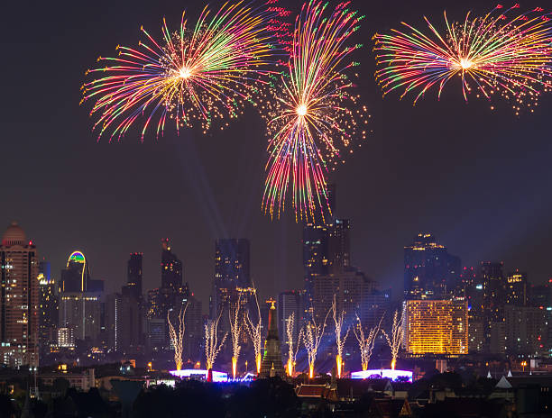 A colorful fireworks burst over illuminated city skyline at night, festive celebration atmosphere fills urban scene of Vijit Chao Phraya 2025 lighting extravaganza opens in Bangkok, Thailand. Public event.