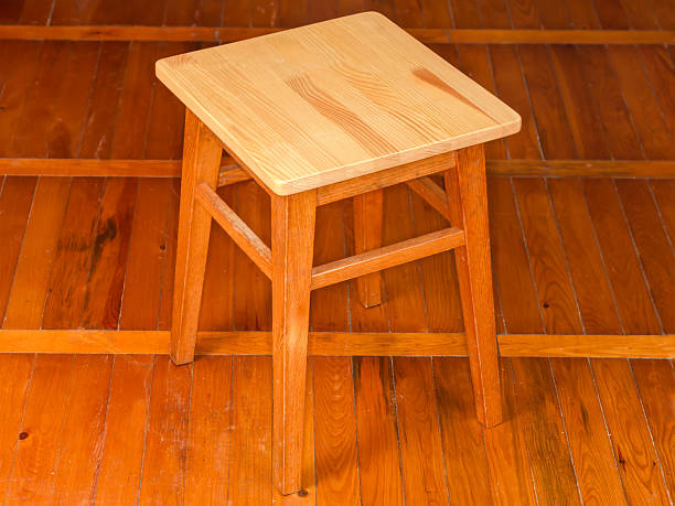 Two rustic wooden stools sit on a gravel base, surrounded by lush greenery, ideal for casual outdoor seating in a natural and inviting environment.
