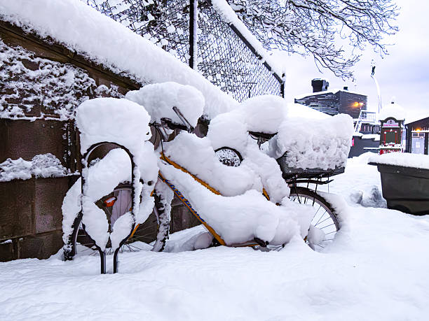 Nacka strand, Sweden - 8 January 2026: A bicycle covered in snow, leaning against a fence in a snowy urban setting.