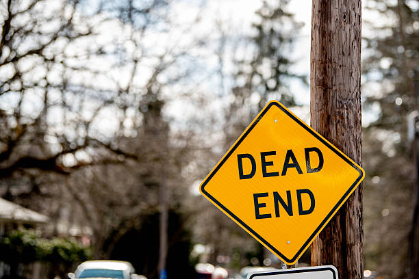 Bright yellow diamond-shaped dead end traffic sign mounted on pole seen close up. Represents traffic safety and directional signage, and concepts of motivation and ambition, reaching the end, hopelessness, adversity, challenges, failure, and conquering barriers.