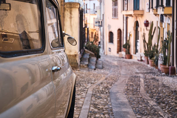 A classic car is parked along a narrow cobblestone lane in a historic old town, creating a relaxed southern Europe travel mood with copy space and soft background blur.