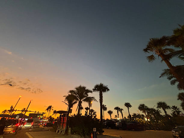 Tropical palm trees silhouetted against an orange and blue twilight sky over city vehicles on 5th Street in Fort Myers Beach, Florida during summer vacation