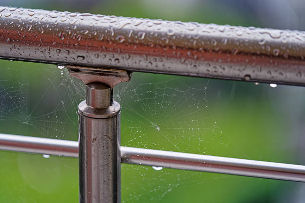Spiderweb With Water Droplets On Metal Balcony Railing