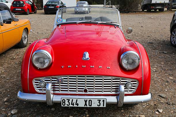 Felixstowe, Suffolk, England - May 04, 2025: Classic red and white Triumph Spitfire car parked on seafront promenade beach and sea in background
