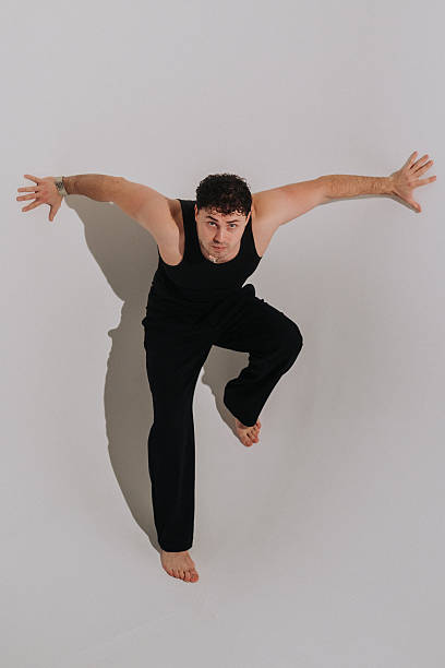 male performer crouched in dynamic pose, intense gaze and poised jump ready for explosive motion, barefoot studio action