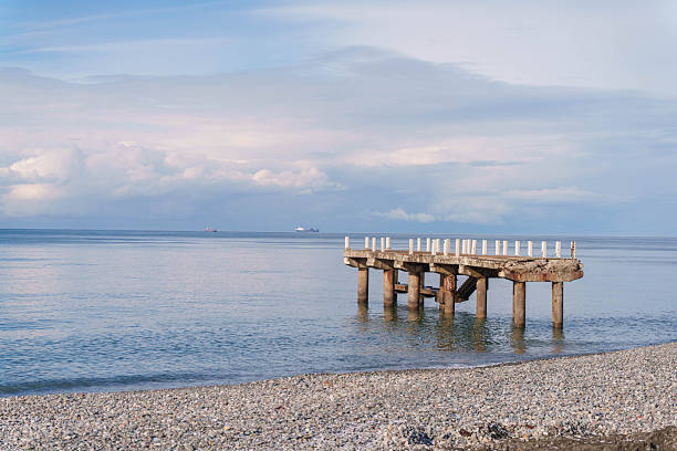 Damaged pier stretching into sea with ships on the horizon. High quality photo