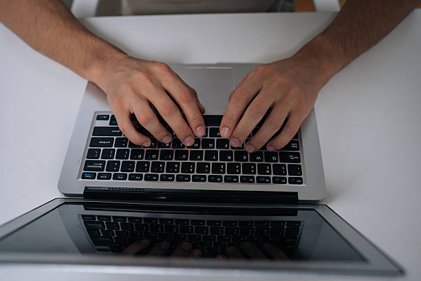 Hands of a woman busy typing on a laptop with a customizable green screen at a desk