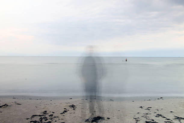 A person in hoodie in silhouette standing by the sea watching it.