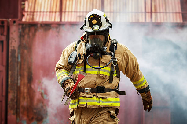 Firefighter wearing a breathing mask and protective uniform standing in heavy smoke during an emergency operation. Concept of firefighting, air protection, hazardous environment, emergency response, safety equipment, and professional rescue service.