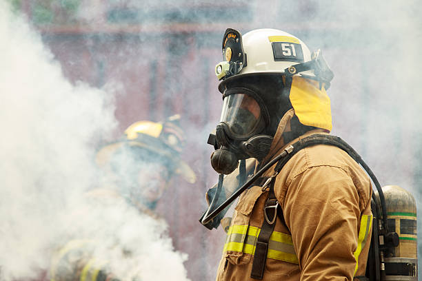 Firefighter wearing a breathing mask and protective uniform standing in heavy smoke during an emergency operation. Concept of firefighting, air protection, hazardous environment, emergency response, safety equipment, and professional rescue service.