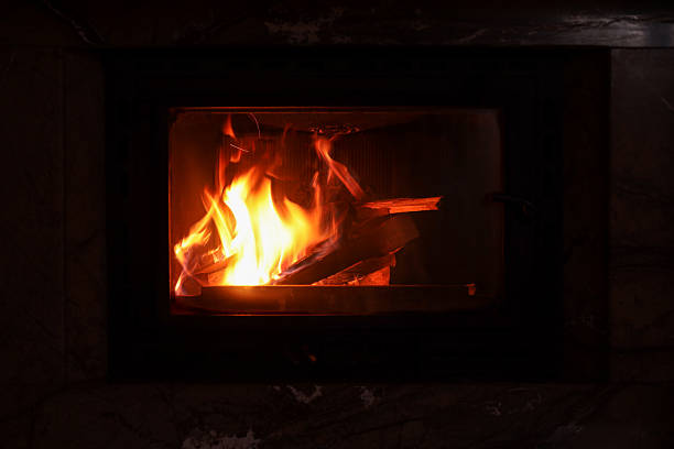 A person placing firewood into a wood-burning stove to keep the fire alive
