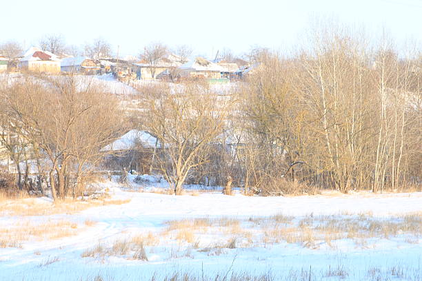 Typical Russian village among the winter forest. Lots of snow, sun and frost. Smoke rises from chimneys. View of the village from the car window. Russian landscape.