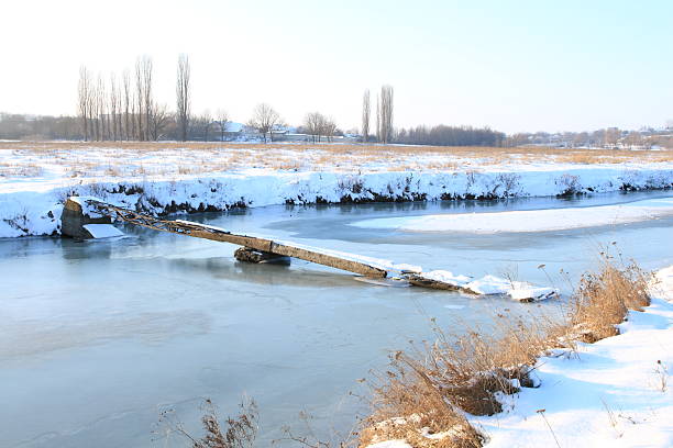 A frozen river with a bridge in the distance. Outdoor. Water. Sky. Nature. Shore
