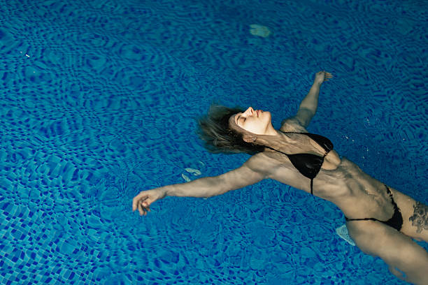 Beautiful woman wearing a bikini is relaxing in an indoor pool. She is floating on water.