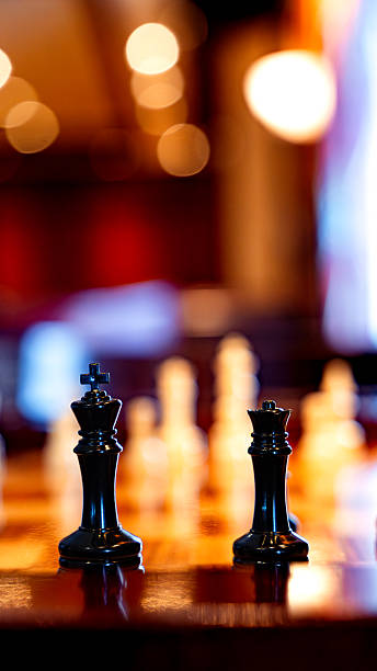 Black chess king and queen pieces standing on a wooden board with blurry background
