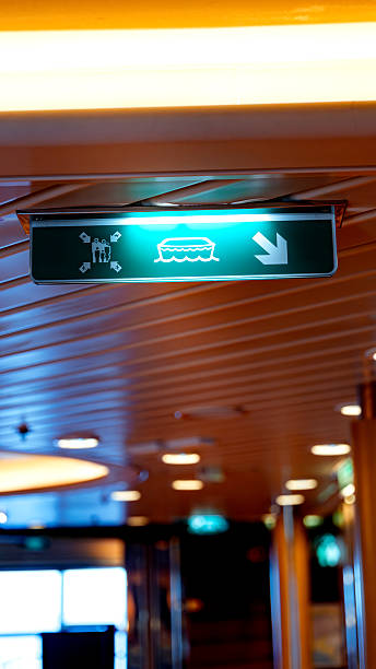 Glowing green sign indicating direction to lifeboat muster station on a cruise ship