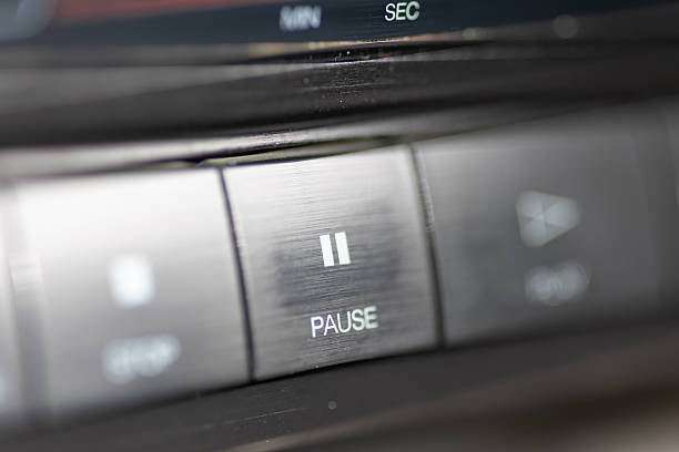 A close-up view of a car stereo featuring a prominent pause button, showcasing sleek metallic controls and a blurred dashboard. Ideal for themes of music, technology, and automotive interiors.