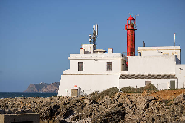 Cascais, Portugal - January 07, 2026: Red lighthouse and white buildings on a rocky coast under a clear blue sky