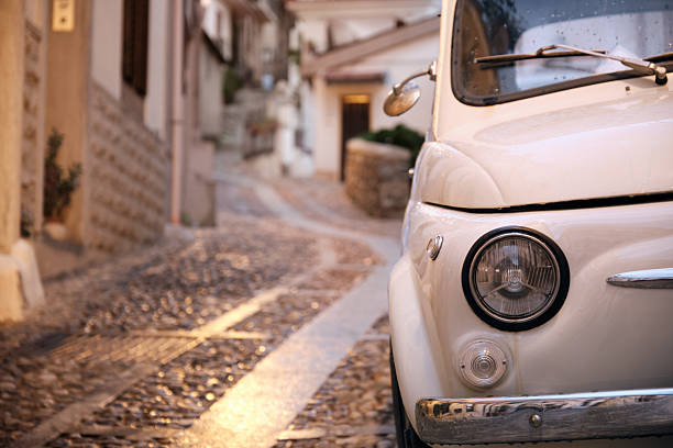 A classic car is parked along a narrow cobblestone street in a historic old town, lit by warm evening light and offering copy space for travel and lifestyle concepts.