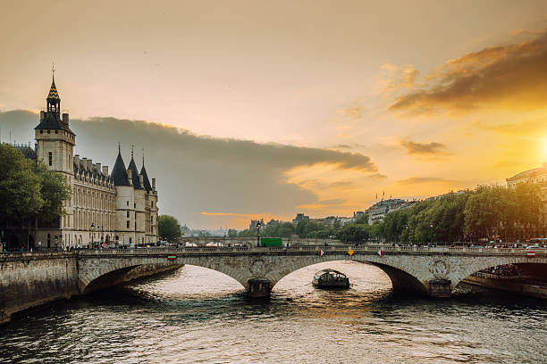 Golden sunset over the Seine River in Paris, featuring a stone bridge and classic Parisian architecture along the embankment. Calm water and warm tones convey a serene, romantic city scene.