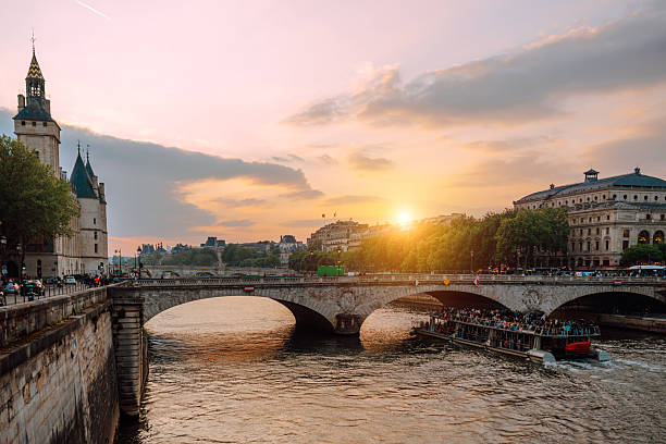 Golden sunset over the Seine in Paris, with a historic stone bridge and boat tour gliding beneath. Classic cityscape featuring river, architecture, and warm evening light.