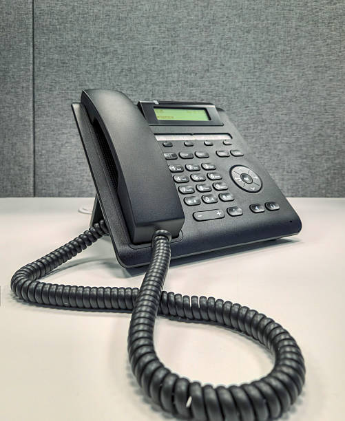 Black desk phone, black office phone on a white desk with a gray background.