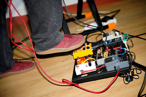 Blank orange guitar pedal with purple knobs and plugged jacks on wooden floor