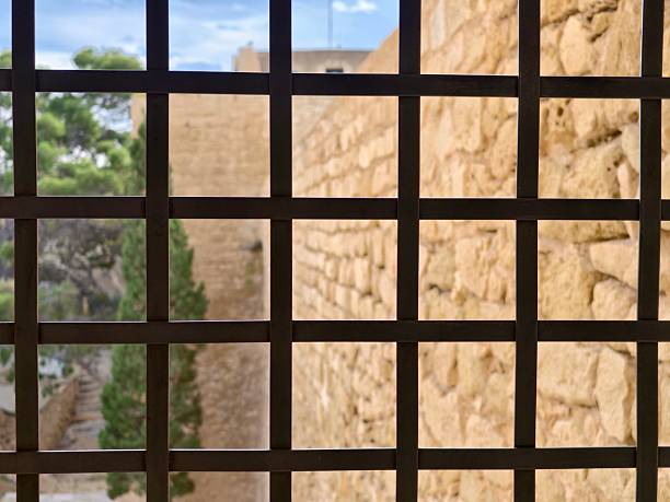 iron grid in foreground with blurred stone outlook beyond, rigid geometry contrasts organic masonry, closeup