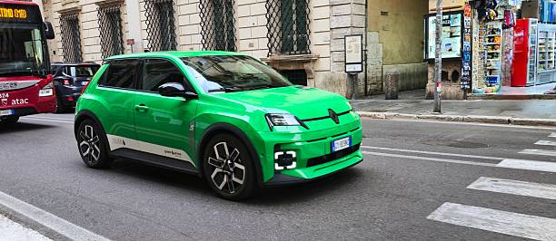 A green Renault 5 E-Tech Electric car drives along Via del Corso in central Rome, with an ATAC city bus in the background, illustrating urban traffic and electric mobility. Modern urban scene highlighting eco-friendly transportation, street life, and contemporary automotive design.