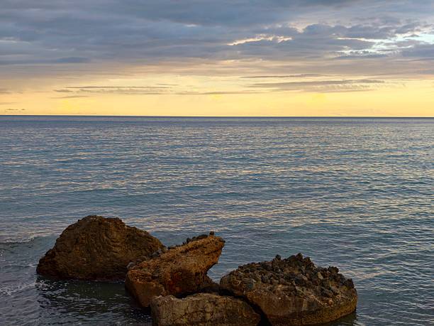 close foreground rocks on quiet shoreline with calm sea and distant clouds, tactile textures and natural