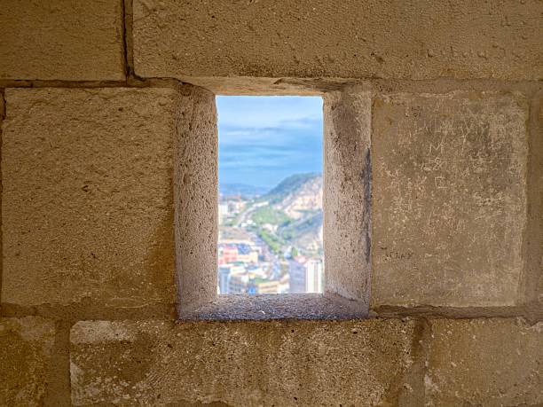 sea view through stone window framed by thick sandstone wall, distant sunlit coastal town with terracotta
