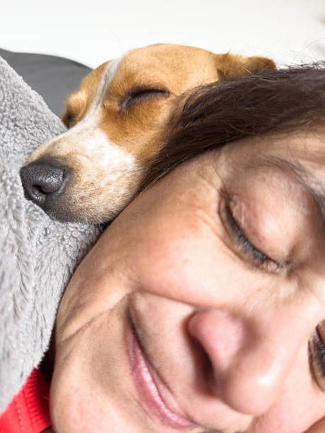 Woman and her dog asleep together on the couch, cuddling close in a cozy, peaceful moment that shows warm companionship, trust and quiet affection at home