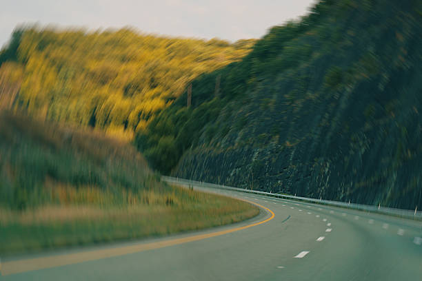 Abstract motion blurred view of a curved highway at sunset, creating a strong sense of speed, movement and acceleration. The dynamic perspective and warm evening light symbolize fast-paced life, progress and travel. Ideal for concepts related to transportation or motion.