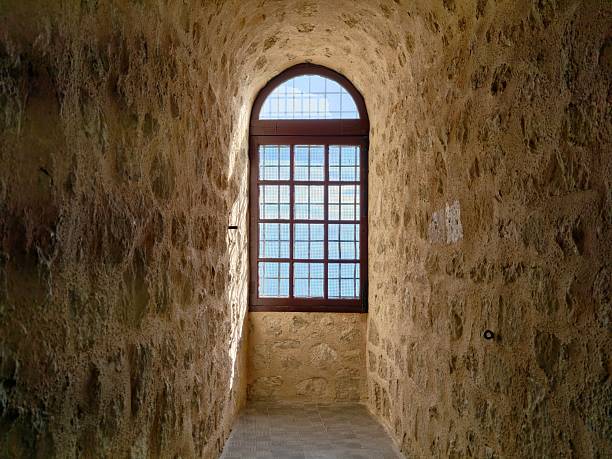 arched window casting warm light down narrow stone corridor, mottled wall texture and soft shadow layers