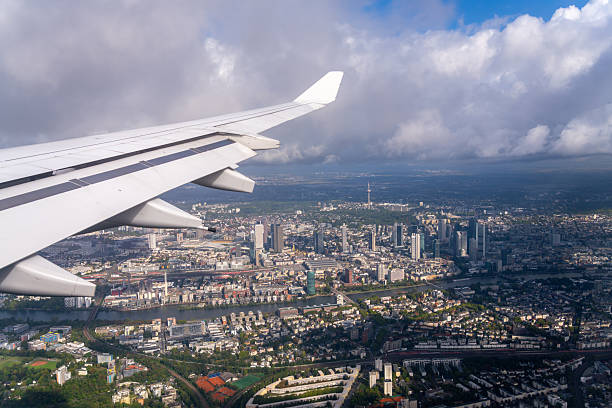 An airplane wing is visible as the aircraft flies over the city of Frankfurt, Germany, with the Main River and skyscrapers in the background.