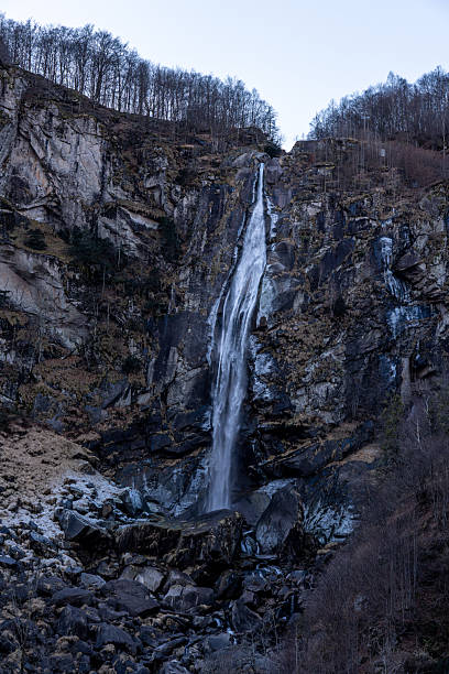 Scenic vertical shot of a high waterfall flowing over dark granite rocks in a bare forest.