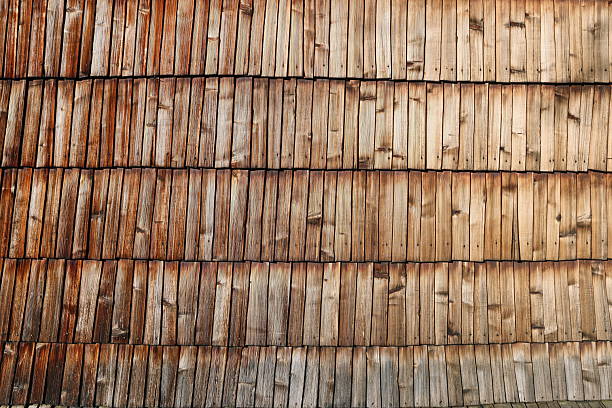 A wooden wall with a pattern of brown and white wood. The wood appears to be weathered and aged, giving the wall a rustic and natural feel. The pattern of the wood is irregular and uneven
