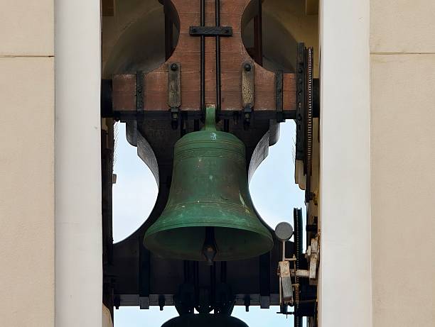 Green bronze bell framed by tower openings, aged patina on metal and wood, wooden yoke and iron supports