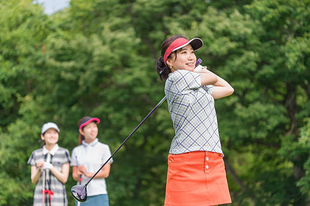 Asian woman swings golf club on golf course