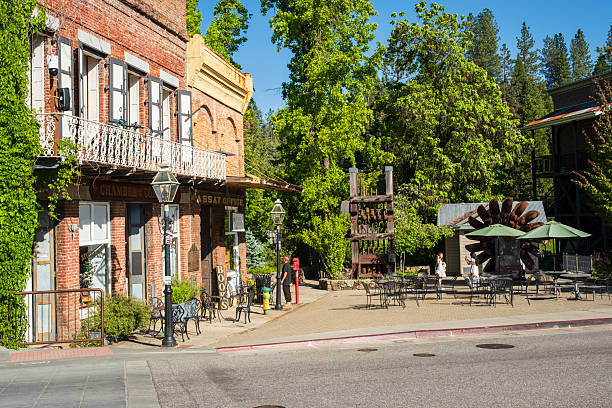 Nevada City, CA - May 19, 2025:  Shops at the end of Broad Street with outdoor seating and antique mining equipment, a Pelton Wheel on the right and stamp mill on the left.