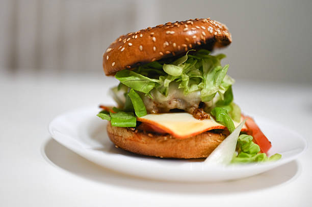 Homemade cheeseburger with beef, cheese, lettuce, tomato, sesame bun, and mustard on white plate