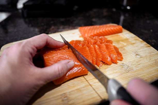 Hand slicing fresh salmon fillet on wood cutting board