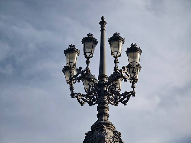 Cast iron streetlight against cloudy sky, ornate filigree and multiple lantern heads, overcast atmosphere