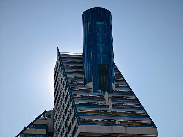 cylindrical glass tower piercing sky, rooftop vertical shaft rising above stepped terraces, dramatic