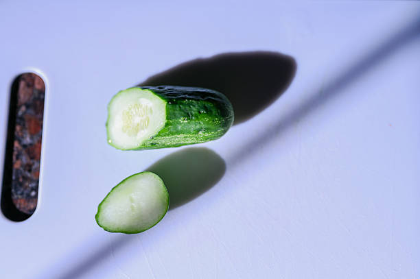 Sliced cucumber pieces hovering with shadows on a white cutting board