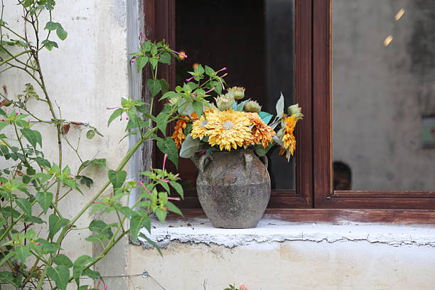 a rustic vase with yellow and orange flowers on the windowsill of an old house in rural italy, in the style of raw photography